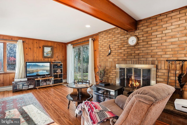 living room featuring beamed ceiling, brick wall, wood-type flooring, wooden walls, and a fireplace