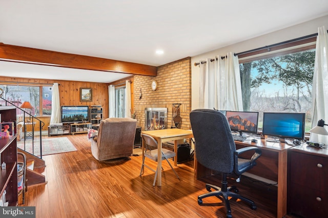 office space featuring beamed ceiling, hardwood / wood-style floors, a brick fireplace, and wood walls