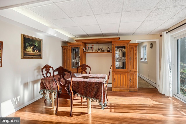 dining space featuring hardwood / wood-style floors, a drop ceiling, and a baseboard heating unit