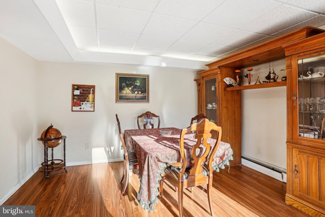 dining area with dark hardwood / wood-style flooring, a drop ceiling, and a baseboard heating unit