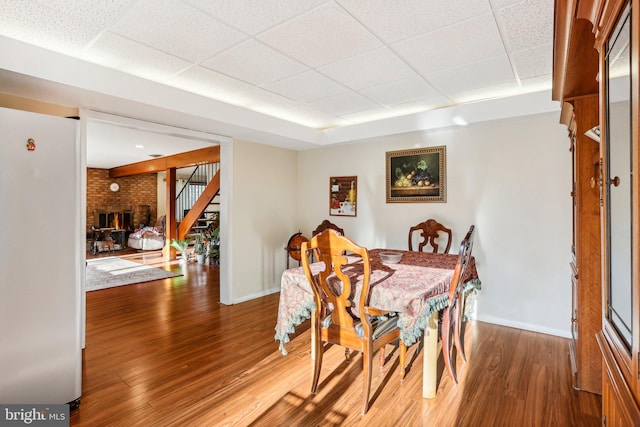 dining space featuring a fireplace, hardwood / wood-style floors, and a drop ceiling