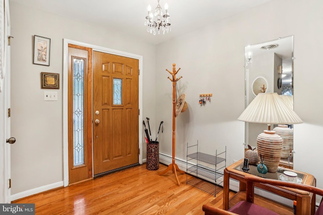 foyer entrance with a baseboard heating unit, light wood-type flooring, and a chandelier