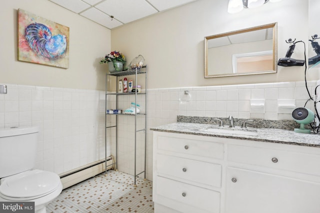 bathroom featuring a baseboard heating unit, toilet, a paneled ceiling, vanity, and tile walls