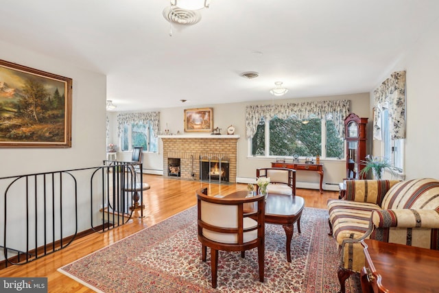 living room with baseboard heating, light hardwood / wood-style flooring, and a brick fireplace