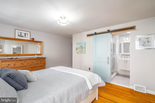 bedroom with a barn door, light wood-type flooring, sink, and ensuite bath