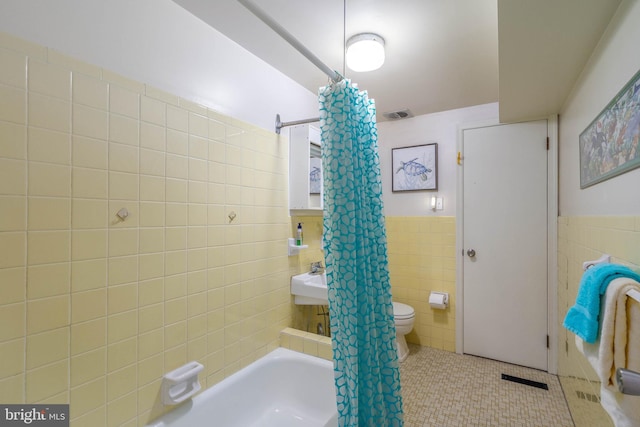 bathroom featuring toilet, tile patterned floors, tile walls, and shower / bath combo with shower curtain