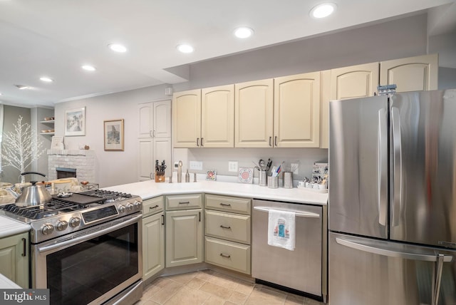 kitchen with a stone fireplace, appliances with stainless steel finishes, and cream cabinets