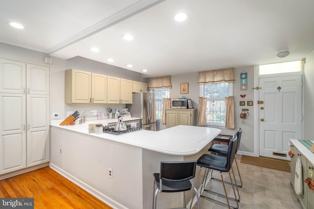 kitchen featuring kitchen peninsula, a breakfast bar, light hardwood / wood-style flooring, and appliances with stainless steel finishes