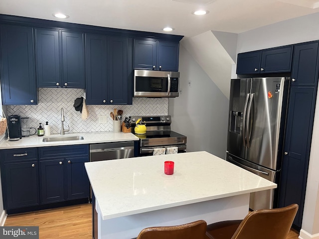 kitchen with sink, blue cabinetry, appliances with stainless steel finishes, light hardwood / wood-style floors, and a kitchen bar