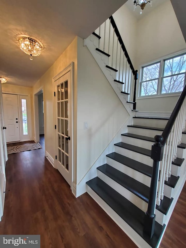 staircase with wood-type flooring, a wealth of natural light, and an inviting chandelier