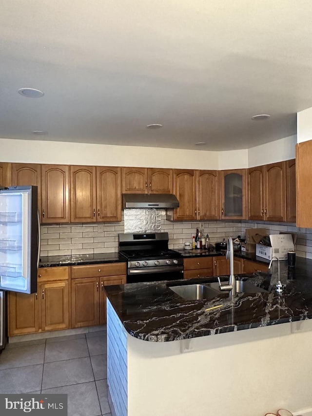 kitchen with dark stone countertops, kitchen peninsula, appliances with stainless steel finishes, and tasteful backsplash