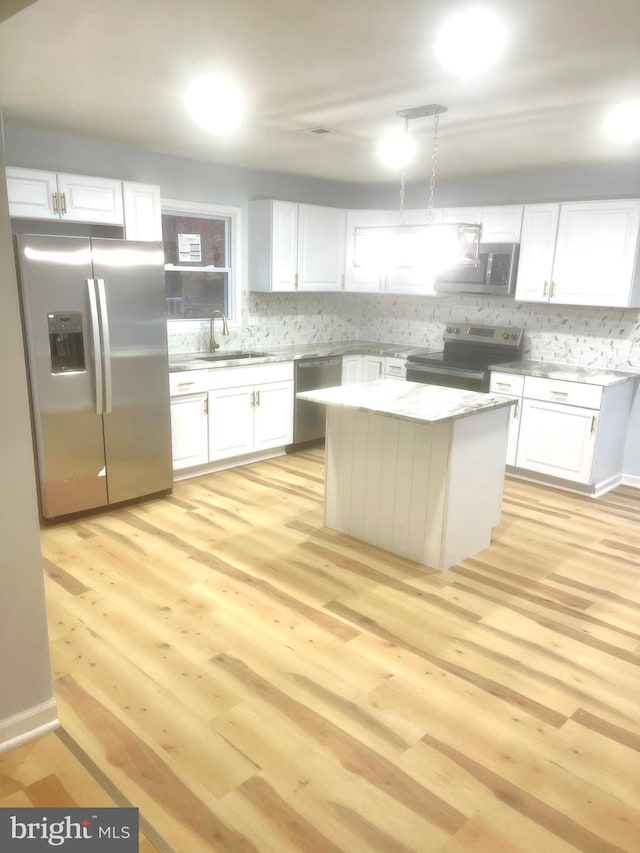 kitchen featuring white cabinetry, a center island, stainless steel appliances, decorative light fixtures, and light wood-type flooring