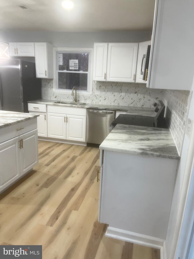 kitchen with white cabinets, light wood-type flooring, stainless steel appliances, and tasteful backsplash