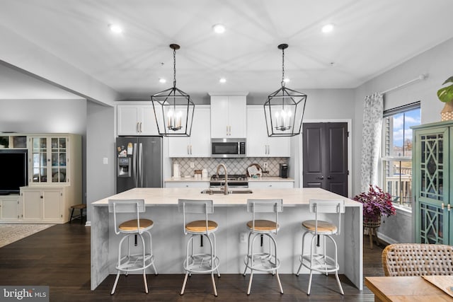 kitchen featuring sink, hanging light fixtures, an island with sink, a breakfast bar, and appliances with stainless steel finishes