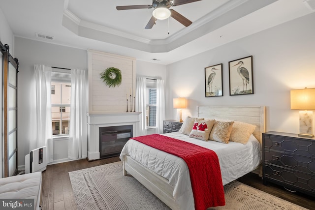 bedroom with dark hardwood / wood-style floors, crown molding, ceiling fan, and a tray ceiling