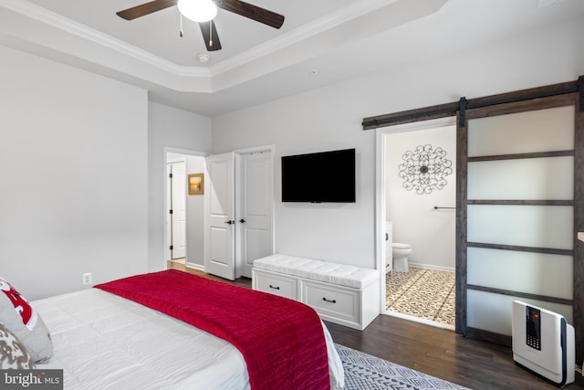 bedroom with ensuite bath, a raised ceiling, ceiling fan, a barn door, and dark hardwood / wood-style floors