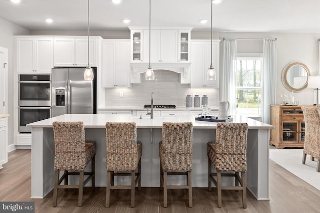 kitchen with a breakfast bar area, an island with sink, pendant lighting, and appliances with stainless steel finishes