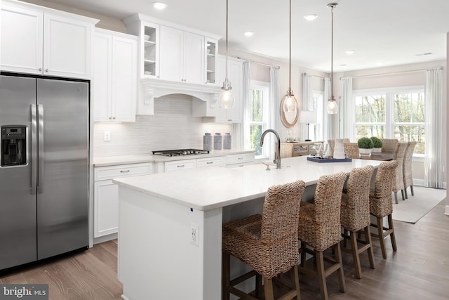 kitchen with hanging light fixtures, stainless steel appliances, an island with sink, a breakfast bar, and hardwood / wood-style flooring