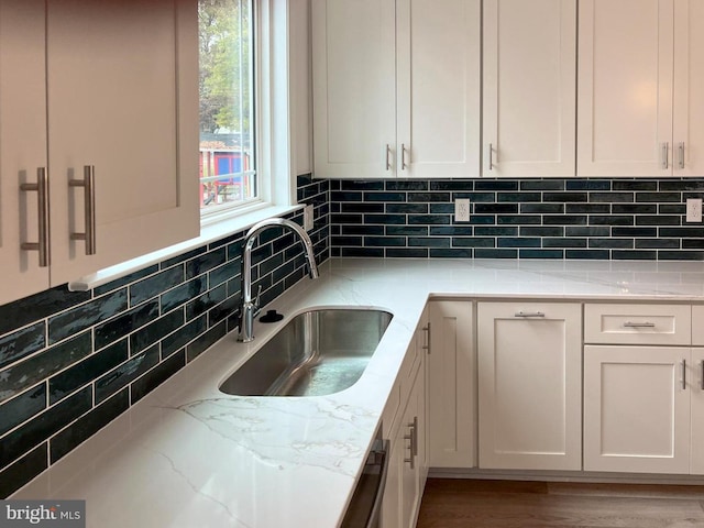 kitchen featuring light stone countertops, decorative backsplash, white cabinets, and a sink