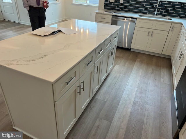 kitchen featuring decorative backsplash, dishwasher, light wood-style flooring, light stone countertops, and a sink