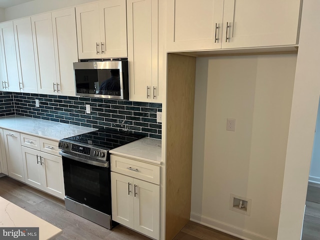 kitchen with tasteful backsplash, light wood-style flooring, appliances with stainless steel finishes, white cabinetry, and baseboards