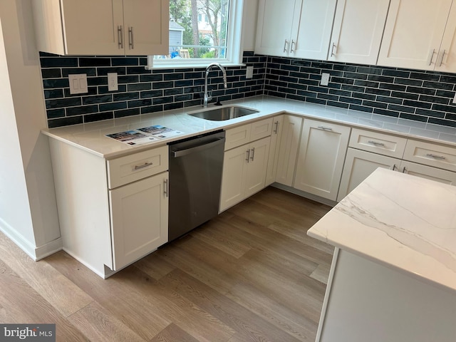 kitchen with light wood finished floors, stainless steel dishwasher, a sink, and tasteful backsplash