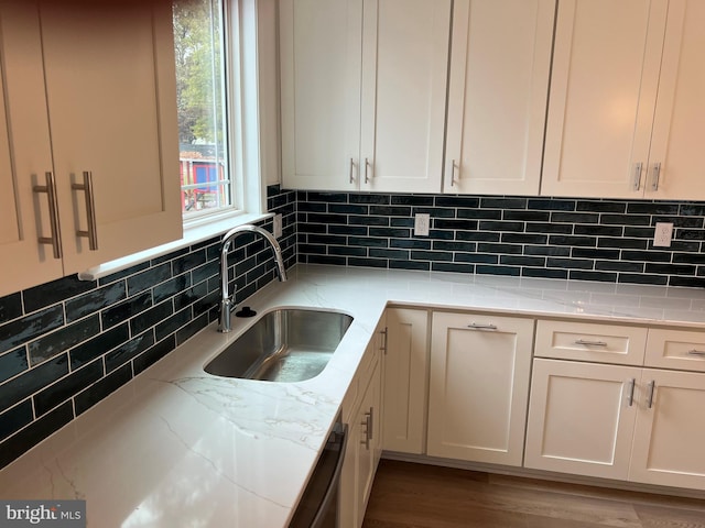 kitchen featuring black dishwasher, tasteful backsplash, light stone counters, white cabinetry, and a sink