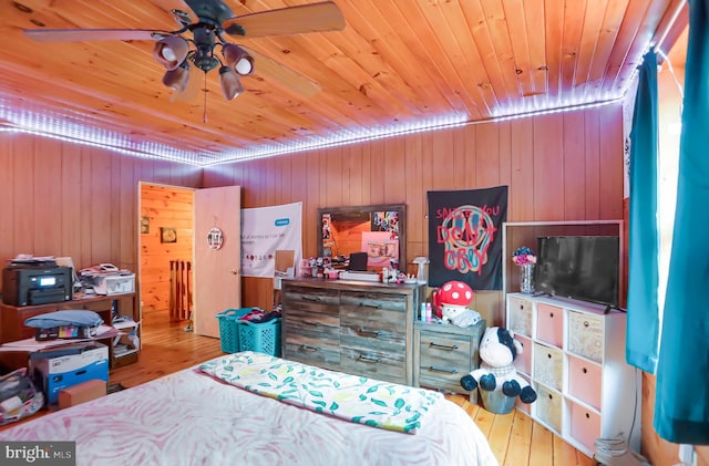 bedroom featuring ceiling fan, light hardwood / wood-style flooring, and wood walls