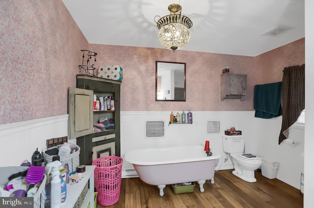 bathroom with toilet, wood-type flooring, a tub to relax in, and an inviting chandelier