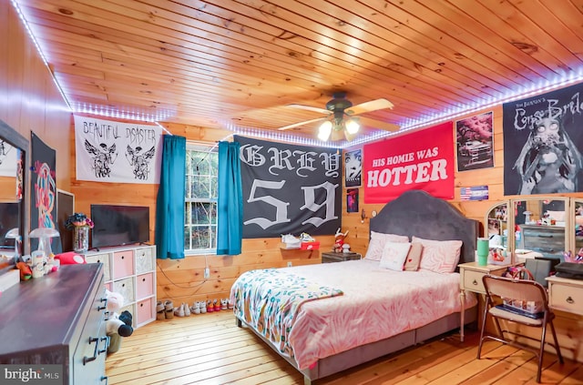 bedroom with ceiling fan, light hardwood / wood-style floors, wooden ceiling, and wooden walls