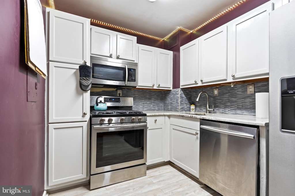 kitchen featuring white cabinets, backsplash, stainless steel appliances, and light hardwood / wood-style flooring