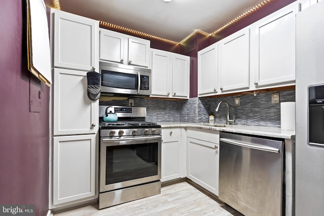 kitchen featuring white cabinets, backsplash, stainless steel appliances, and light hardwood / wood-style flooring