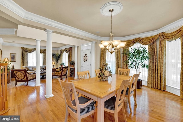 dining area with light wood-type flooring, an inviting chandelier, ornamental molding, and decorative columns