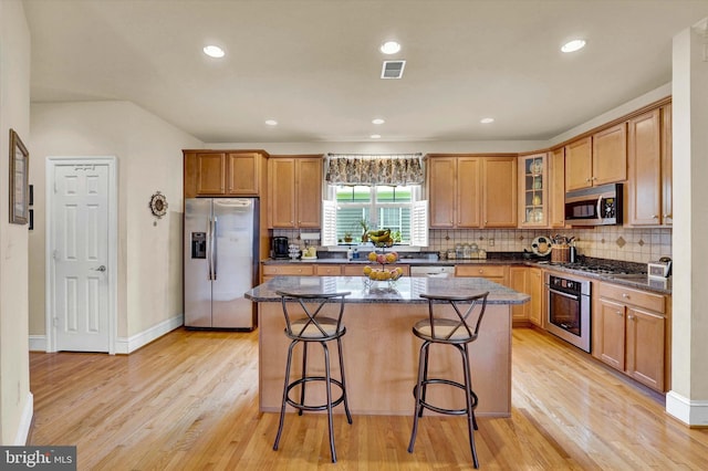 kitchen with a center island, a breakfast bar, light hardwood / wood-style flooring, appliances with stainless steel finishes, and dark stone counters