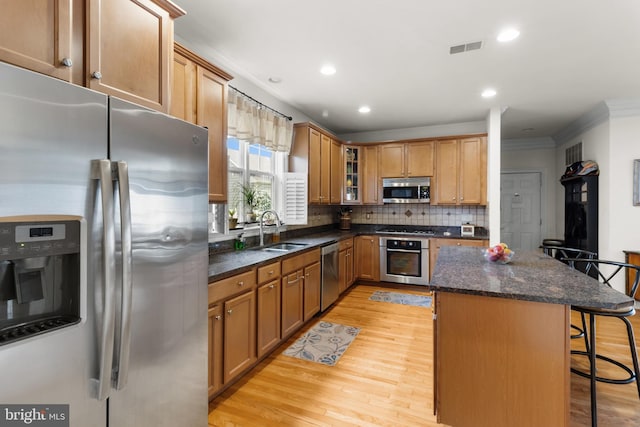 kitchen with stainless steel appliances, dark stone countertops, sink, light wood-type flooring, and a breakfast bar area