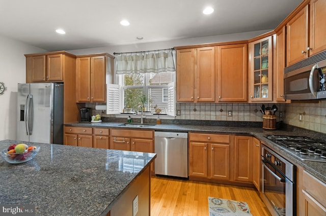 kitchen featuring stainless steel appliances, dark stone countertops, light hardwood / wood-style floors, and sink