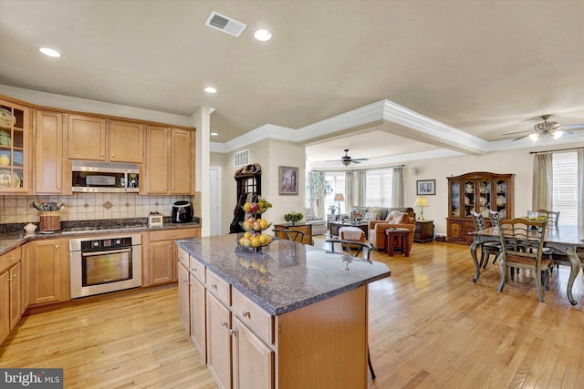 kitchen with a kitchen island, stainless steel appliances, dark stone counters, tasteful backsplash, and light hardwood / wood-style floors