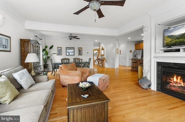 living room with ceiling fan, a high end fireplace, ornamental molding, and light hardwood / wood-style floors