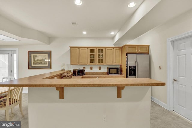 kitchen with stainless steel refrigerator with ice dispenser, a breakfast bar area, light brown cabinetry, and kitchen peninsula