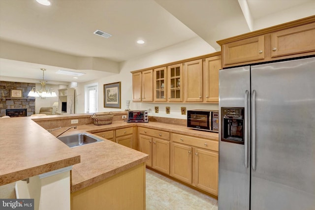 kitchen with stainless steel refrigerator with ice dispenser, decorative light fixtures, a stone fireplace, light brown cabinetry, and sink