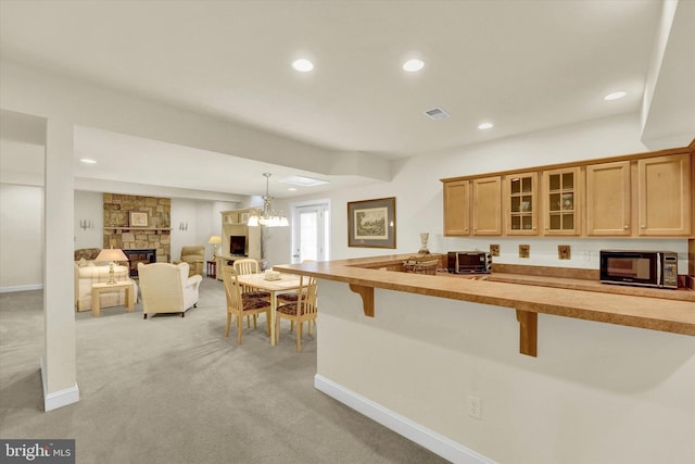 kitchen with a breakfast bar, pendant lighting, light colored carpet, and a stone fireplace