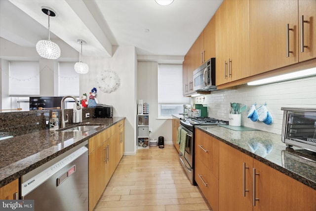 kitchen featuring dark stone counters, stainless steel appliances, sink, decorative light fixtures, and light hardwood / wood-style floors