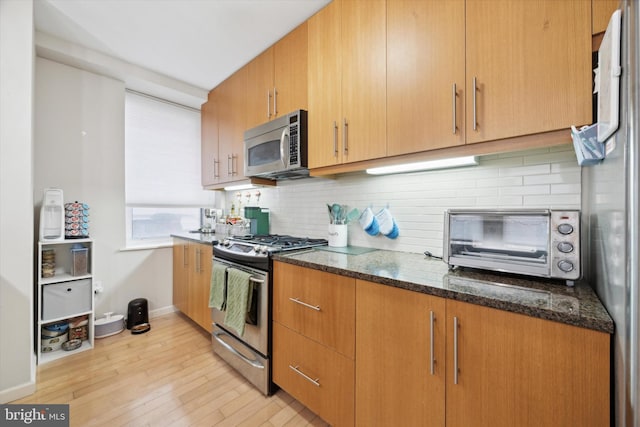 kitchen with decorative backsplash, light hardwood / wood-style floors, appliances with stainless steel finishes, and dark stone counters