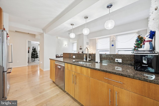 kitchen featuring dark stone counters, sink, light wood-type flooring, appliances with stainless steel finishes, and decorative light fixtures