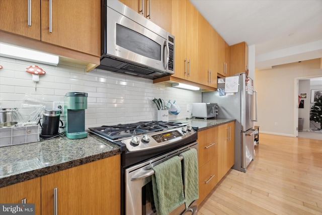 kitchen with decorative backsplash, stainless steel appliances, dark stone counters, and light hardwood / wood-style flooring