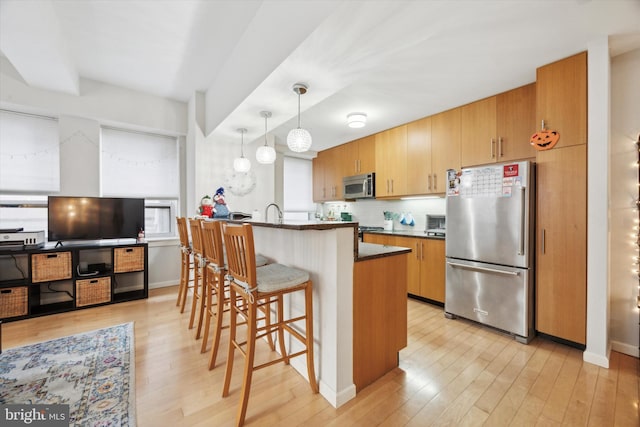 kitchen with light hardwood / wood-style flooring, an island with sink, decorative light fixtures, a kitchen bar, and stainless steel appliances