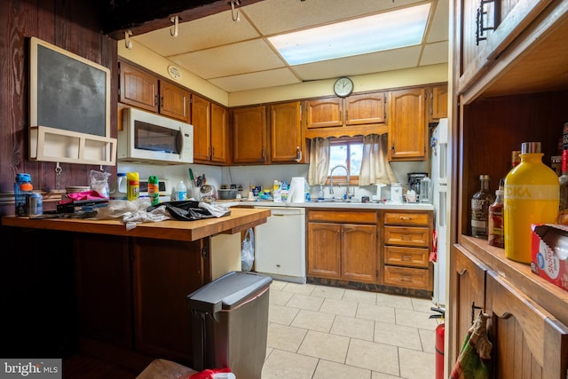 kitchen with a paneled ceiling, sink, light tile patterned flooring, and white appliances