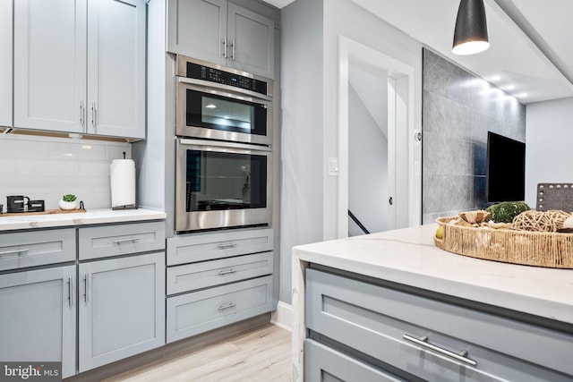 kitchen featuring gray cabinetry, light hardwood / wood-style floors, double oven, and tasteful backsplash