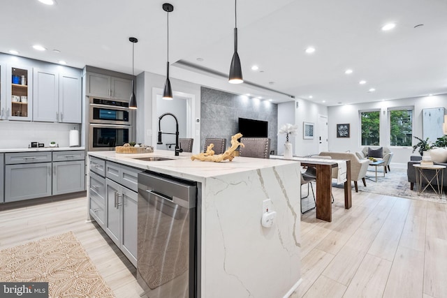 kitchen with sink, stainless steel appliances, light stone counters, an island with sink, and pendant lighting