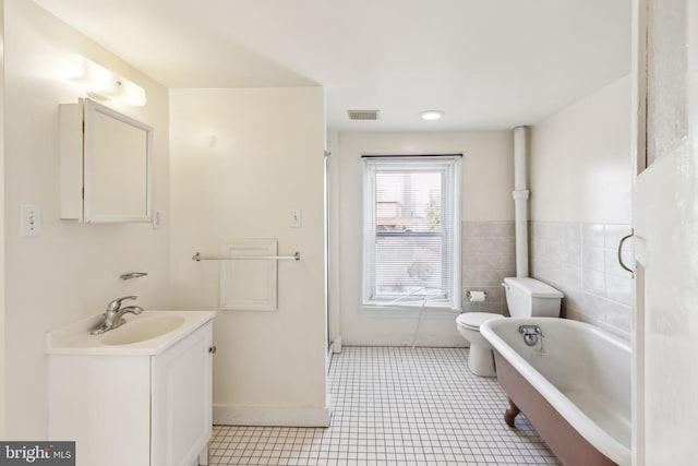 bathroom featuring vanity, a bathing tub, tile patterned flooring, toilet, and tile walls